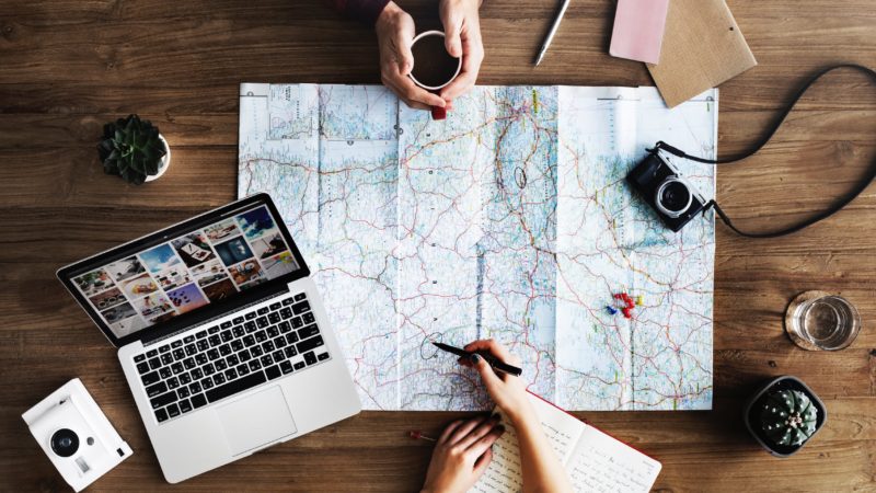 Person Using Map and Laptop on Wooden Surface